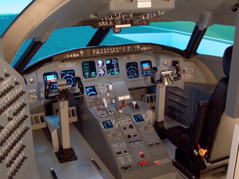 cwu-Simulator consisting of chair, airplane control planels and switches in front of the thair; three monitors showing a simulated runway and blue, partially cloudy sky